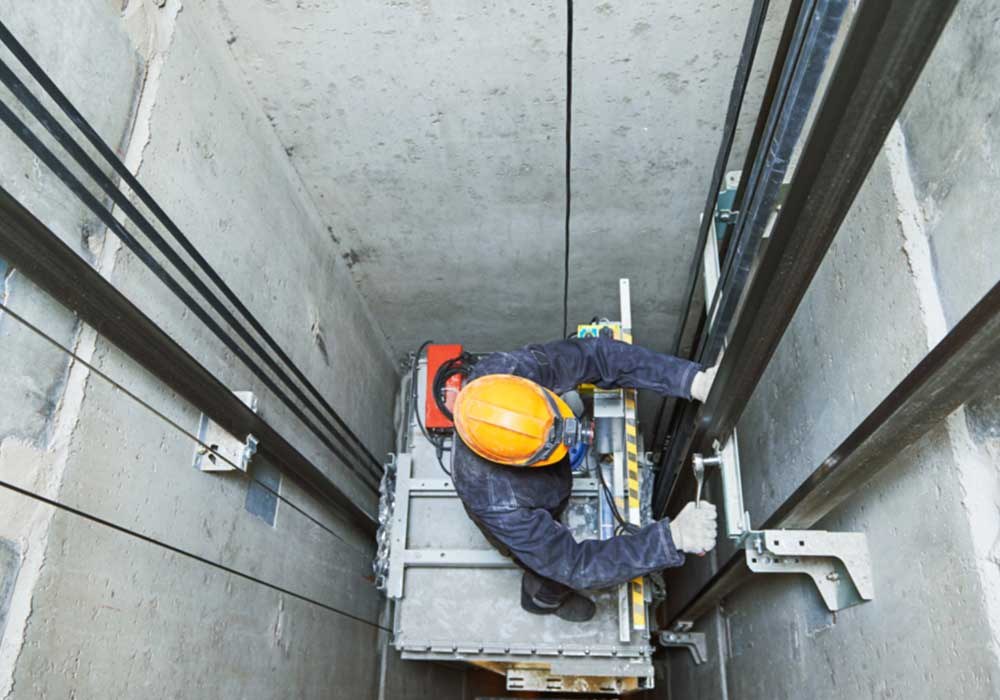 Tecnico ascensorista al lavoro sul tetto della cabina in un vano corsa